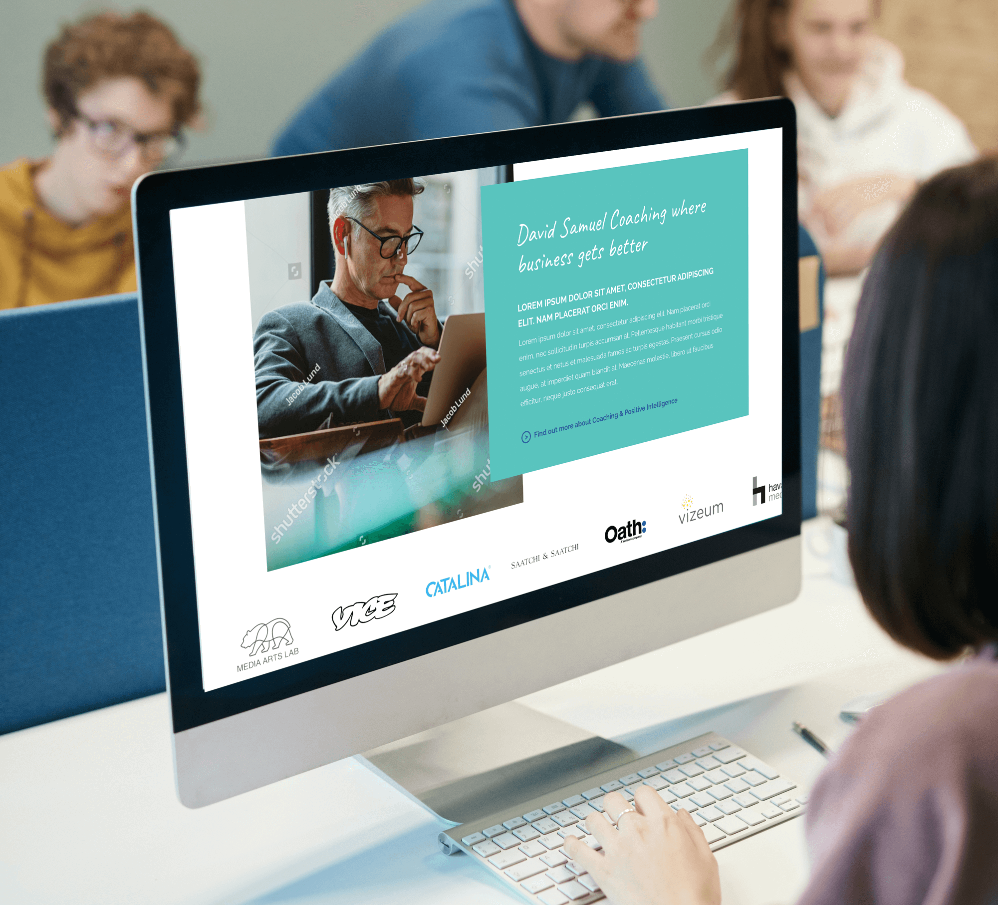 Desktop computer displaying bespoke business website with turquoise design and coaching content, team members visible in background.