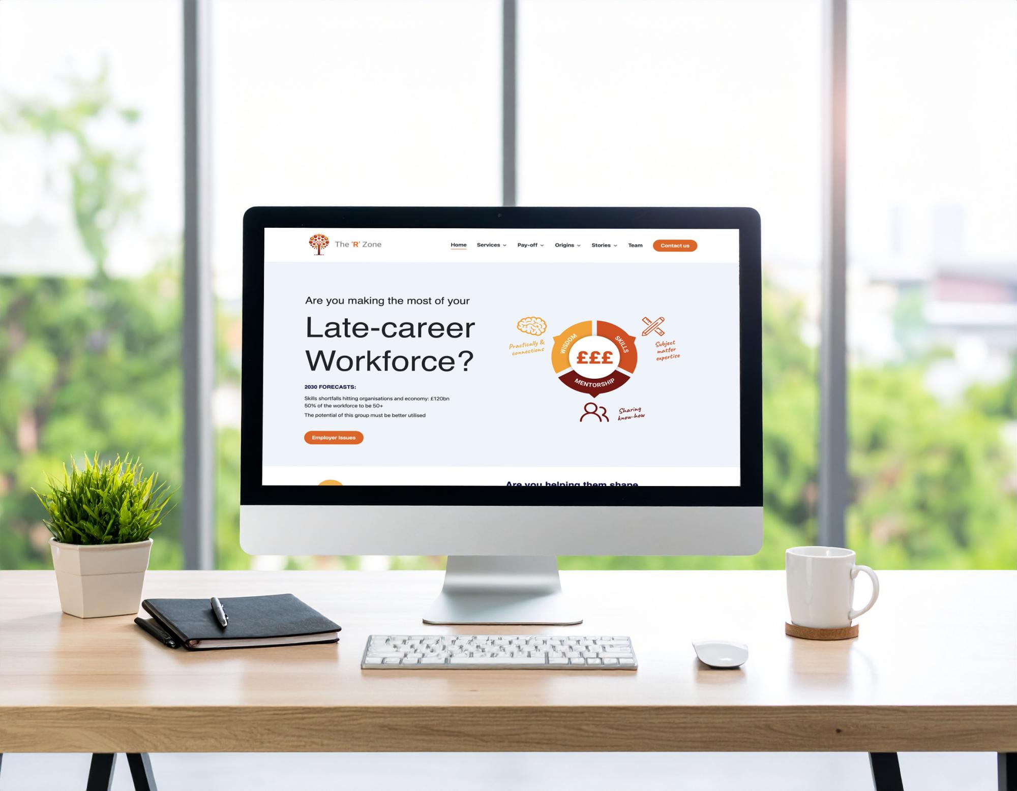 Desktop computer displaying bespoke website for late-career workforce client, sat on desk with notebook and coffee.