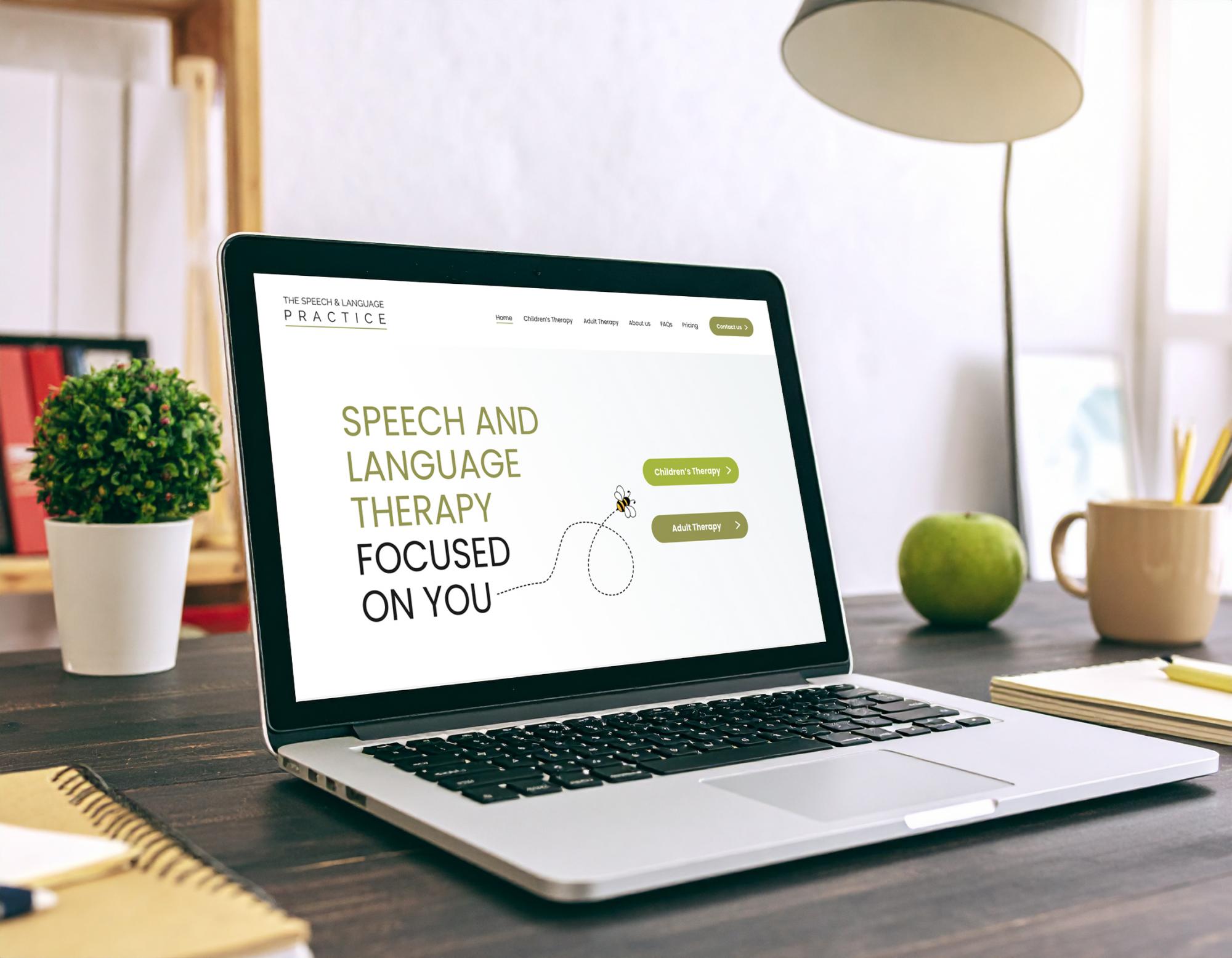 Laptop displaying speech and language therapy practice website homepage on wooden desk with plant and accessories.