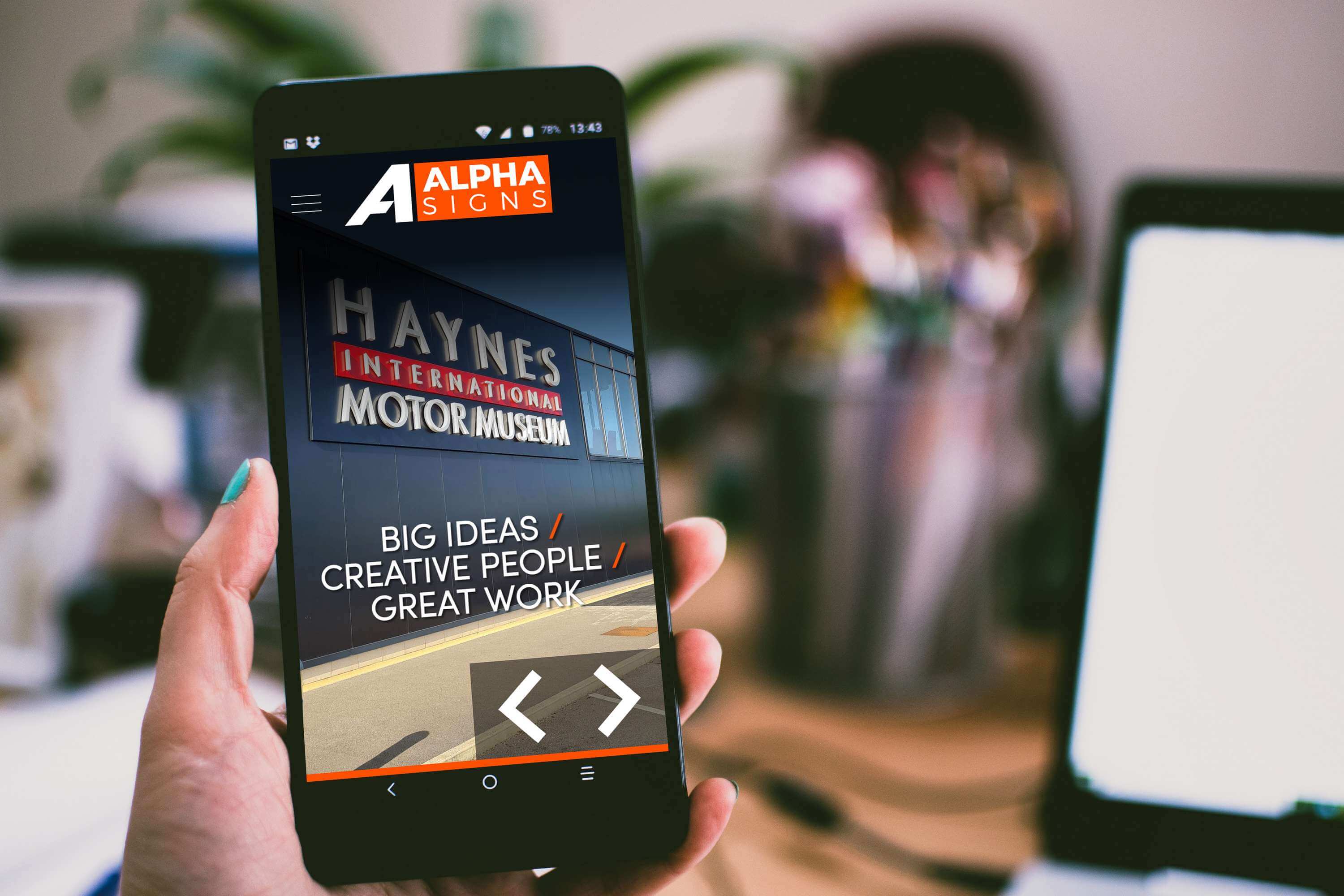 Smartphone displaying Alpha Signs website with Haynes International Motor Museum branding and tagline about big ideas and creative work.